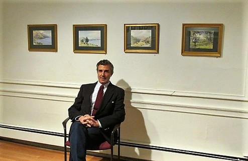 Picture of the artist next to some framed artwork.